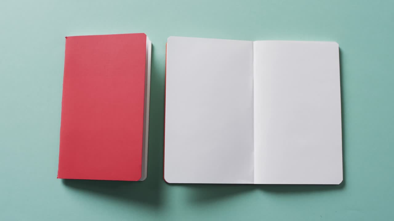 Close up of open blank book and closed red book with copy space on green background in slow motion