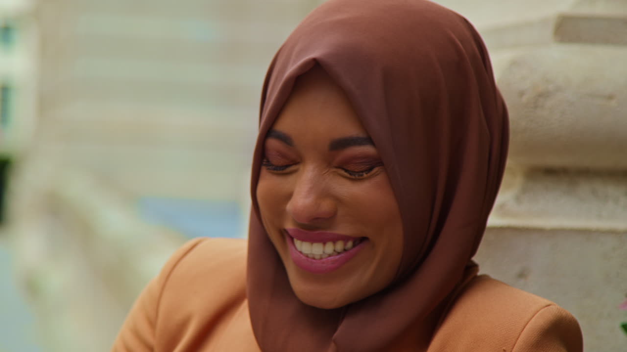 히자브와 현대 비즈니스 슈트를 입은 웃는 무슬림 사업가 여성의 근접 초상화 도시 사무실 건물 밖에서 서 있습니다.