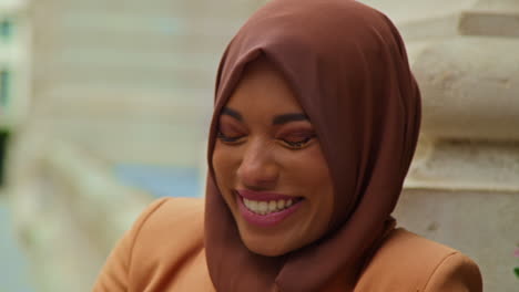 close up portrait of smiling muslim businesswoman wearing hijab and modern business suit standing outside city office buildings