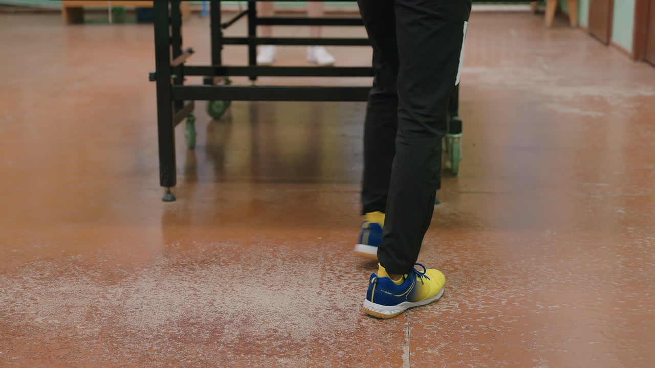 Leg view of tennis players on indoor court showing one in black trouser with yellow shoes and another in shorts focusing on stance movement positioning and agility