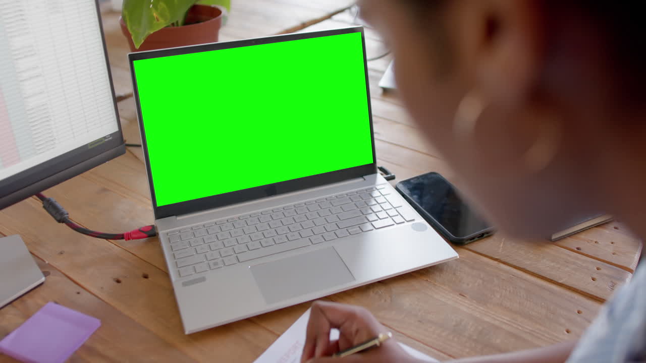 African american businesswoman using laptop with green screen and writing notes, slow motion