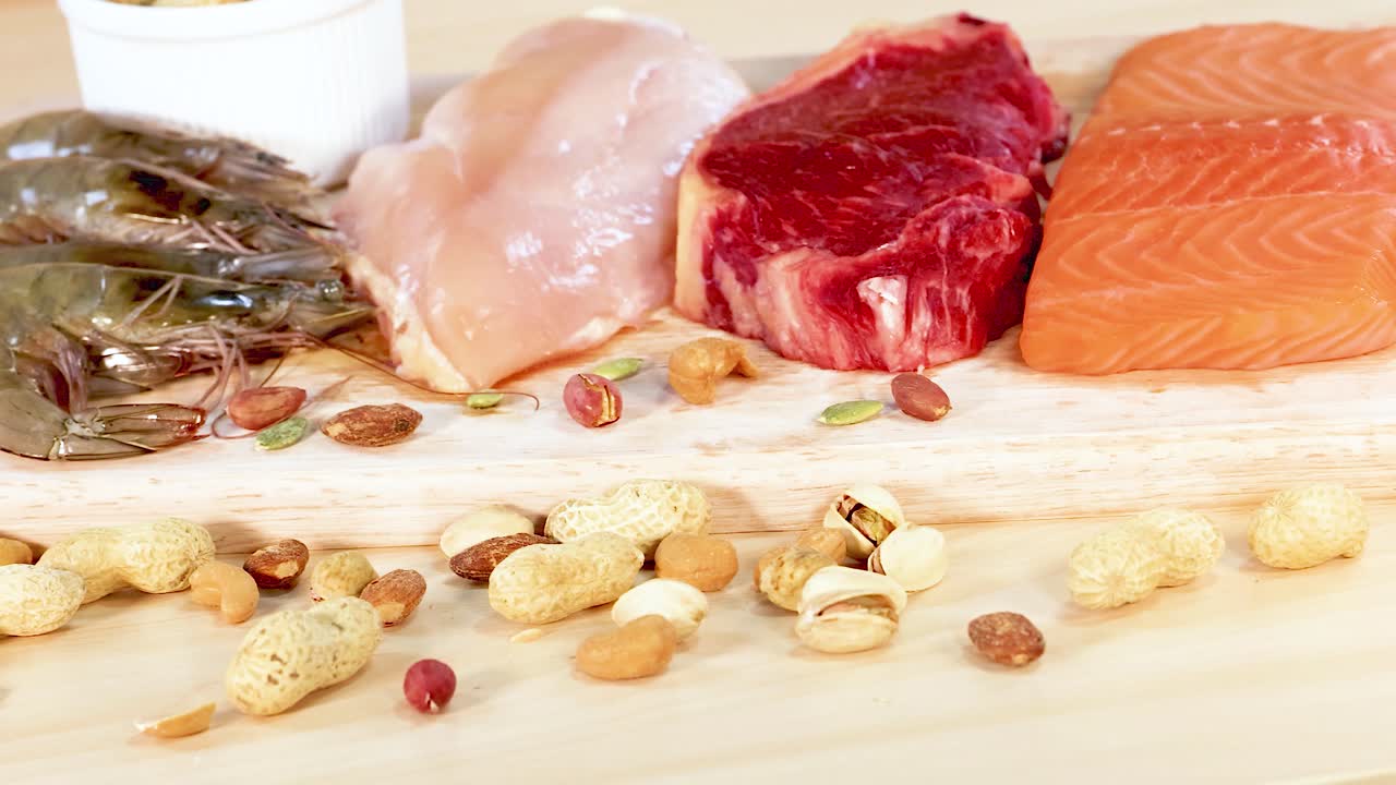 A variety of protein-rich foods including meats, nuts, and dairy are artfully arranged on a wooden surface