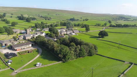 drone footage reversing and panning showing rural yorkshire countryside, revealing a small country village and campsite, including farmland, dry stone walls and ingleborough mountain in the distance