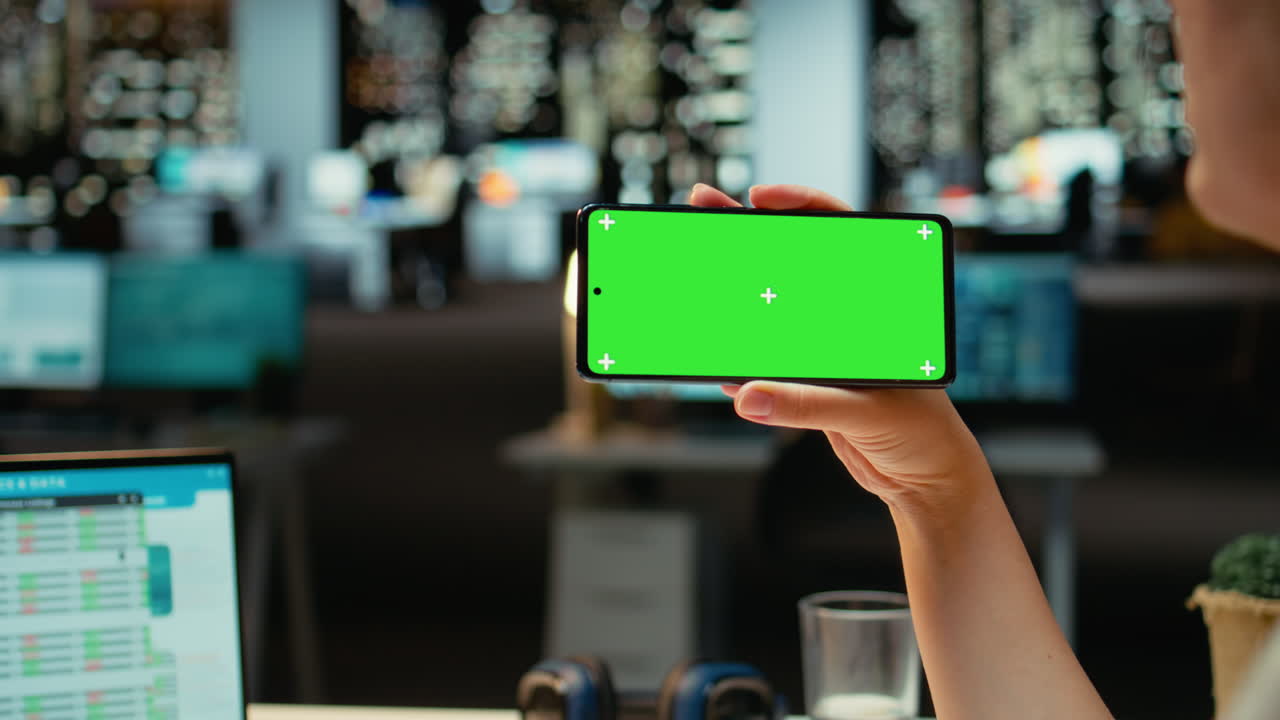 Video verticale. Donna che tiene in mano uno smartphone con mockup isolato dello schermo in un ufficio buio