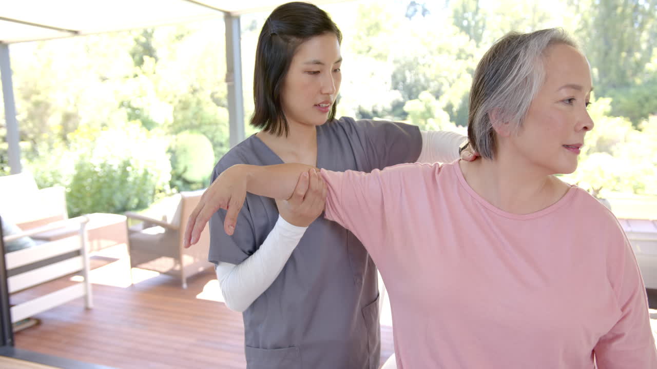 Physical therapist assisting senior asian woman with arm exercises at home