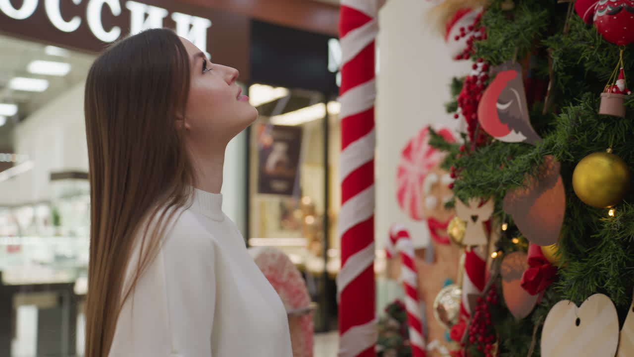 Young woman walking towards decorative plant in modern shopping mall, with long flowing hair, bright and stylish atmosphere with retail displays and glass cabinets in background