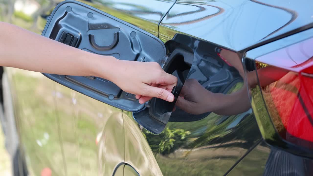 A person refuels a vehicle at a gas station in Phuket, Thailand, under bright daylight, highlighting the refueling process