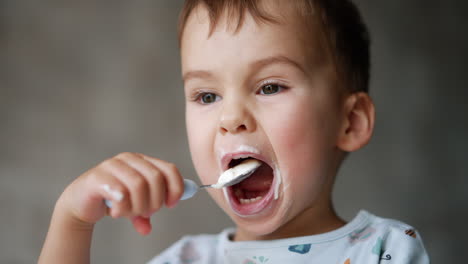 lovely caucasian baby enjoying tasty yogurt. cute kid portrait with dairy all over his mouth. close up.