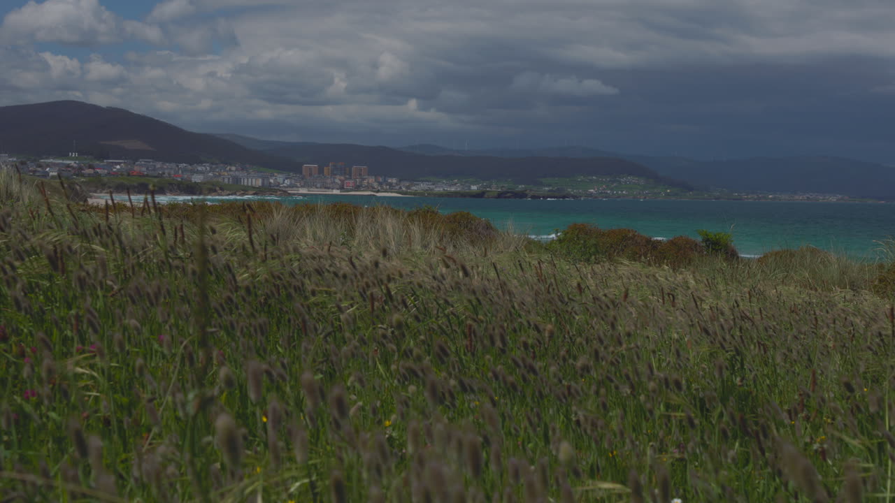Vista dalla scogliera della costa settentrionale spagnola con onde oceaniche e una città sullo sfondo.