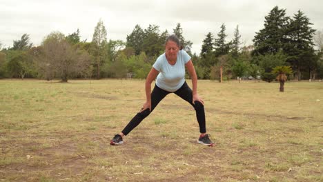 mujer madura haciendo estiramiento de adductor de pie en un parque público abierto