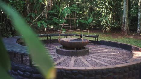 circular bench seating surrounds an empty grill structure in a serene, lush tropical forest, creating a peaceful outdoor retreat