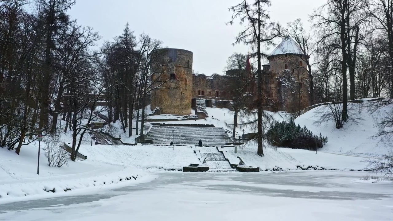 Historialliset Cēsisin linnan rauniot Latviassa, lumipeitteisen puiston ja jäätyneen järven ympäröimänä, ilmakuva.