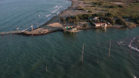 Aerial-shot-of-the-valleys-near-Ravenna-where-the-river-flows-into-the-sea-with-the-typical-fishermen's-huts-at-sunset