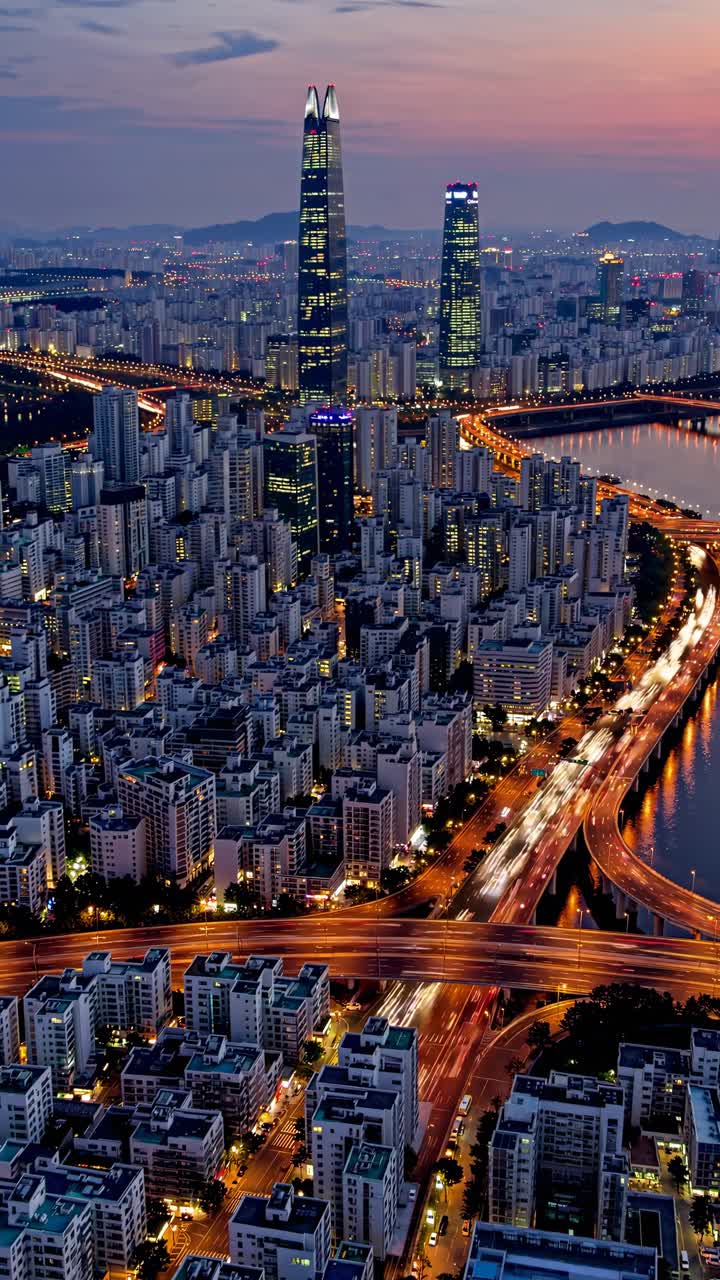 Vista aerea di un vivace paesaggio urbano al tramonto, che mostra grattacieli illuminati e strade tortuose.