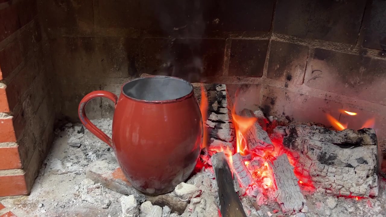 Una olla roja reposa sobre brasas incandescentes en una chimenea rústica, con humo ascendiendo suavemente. Ideal para temas de cocina tradicional o ambientes hogareños acogedores.