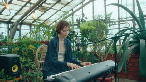female musician playing keyboard and enjoying melody in greenhouse