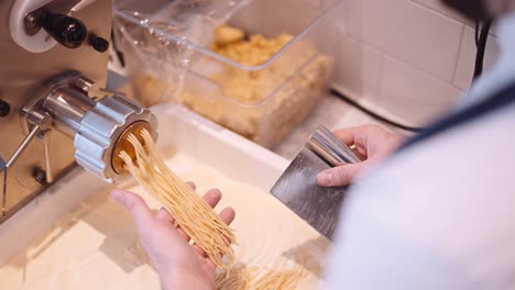 Männlicher-Koch-Schneidet-Die-Langen-Spaghettistränge-Aus-Der-Nudelmaschine