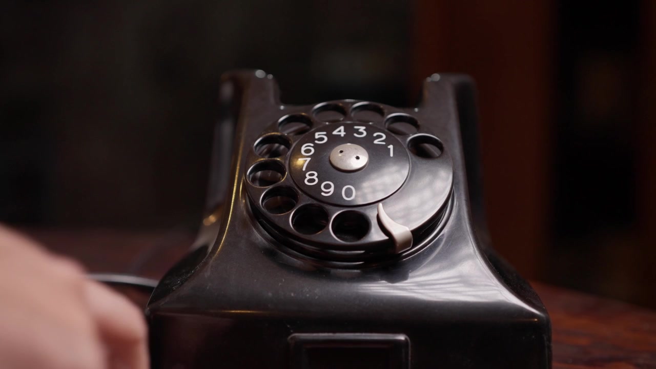 Tangan mengoperasikan dial bernomor telepon putar vintage hitam di atas meja kayu, memutar nomor dengan cepat lalu menutup telepon, zoom out