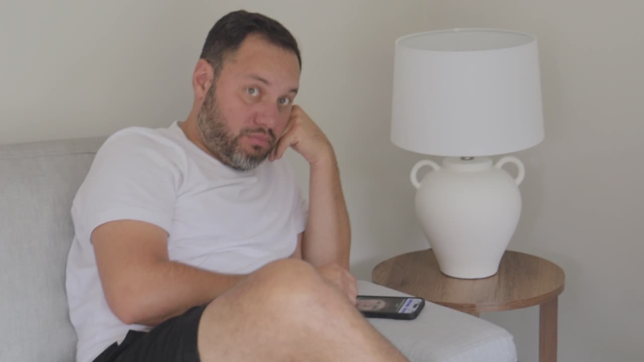 Uomo annoiato che riposa sul divano mentre guarda il suo telefono.