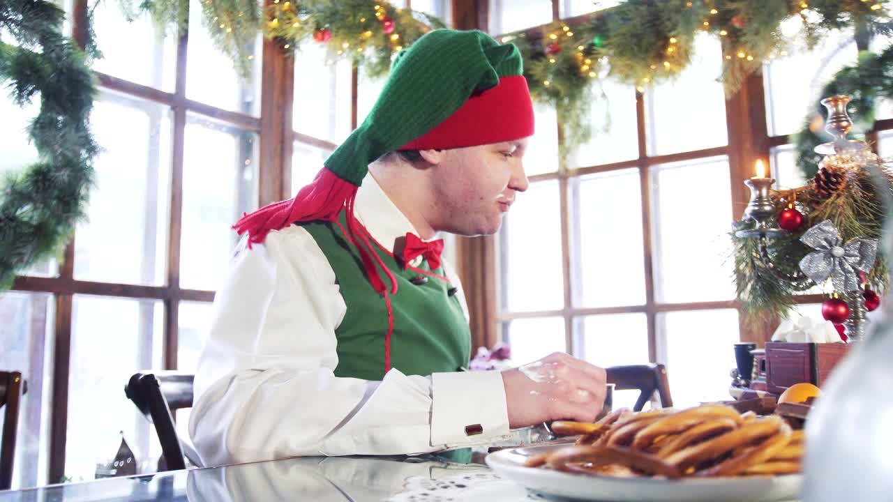 Hungry elf with dirty face and hand eating at the table. Funny man in elf costume quickly eats at Christmas