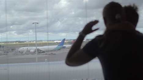 back view of mother and son standing and watching in the window on the airplane runway amsterdam netherlands