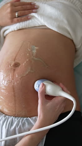 pregnant lady lies on the doctor's couch and her husband sits beside. obstetrician's hand moves the sensor by the big belly of expecting woman. vertical video