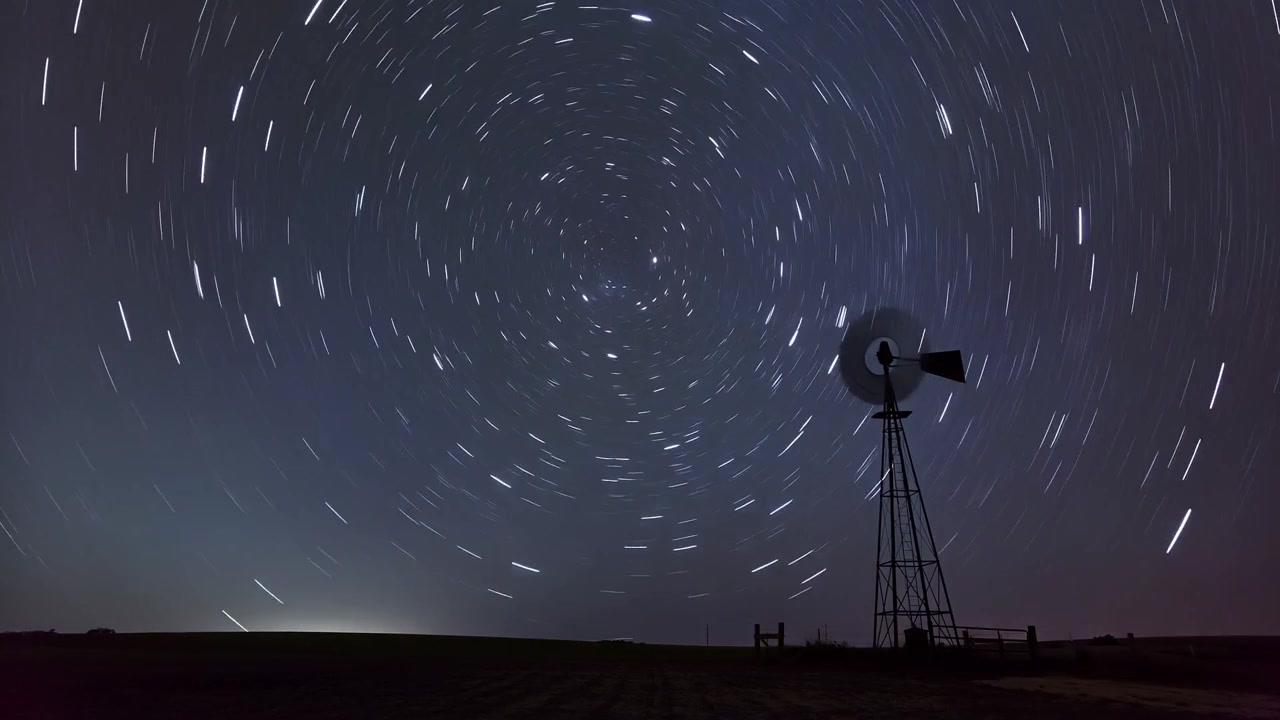 Capturing sunset fading, metal windmill rotating rotor over field, forming star trails, copy space