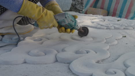 sculptor in workwear grinding white marble stone with drill machine at the working space, da nang city, vietnam, close-up shot