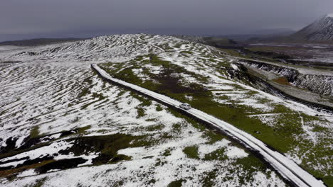 Aerial:-Side-follow-of-one-car-driving-in-the-hills-partially-covered-with-snow