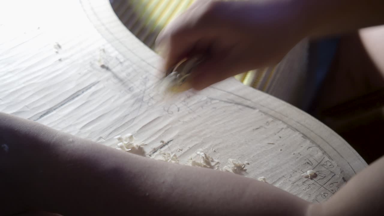 fabricante de instrumentos de cuerda maestro luthier artesano mano proceder con el trabajo de graduación en la placa trasera del violonchelo, dividir la madera en áreas para tallar diferentes espesores con planos, astillas de madera y rizos se amontonan
