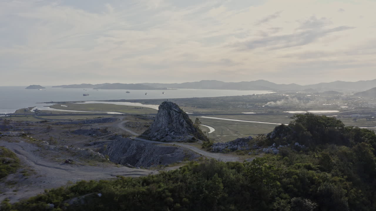 пролет над заброшенным карьером на вершине горы и вид горного хребта вдали, город и корабли на якорной стоянке в заливе в закатное время, съемка с воздуха, россия