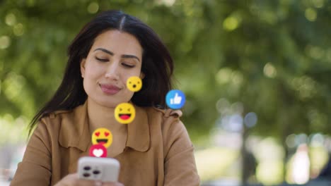 mujer sonriente sentada en una mesa al aire libre mirando un teléfono móvil con emojis de gráficos en movimiento que muestran múltiples notificaciones de redes sociales gustando y reaccionando al contenido en línea