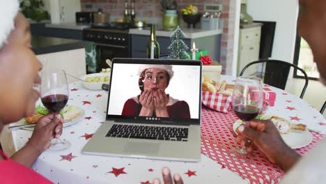 African-american-couple-with-wine-using-laptop-for-christmas-video-call-with-happy-woman-on-screen