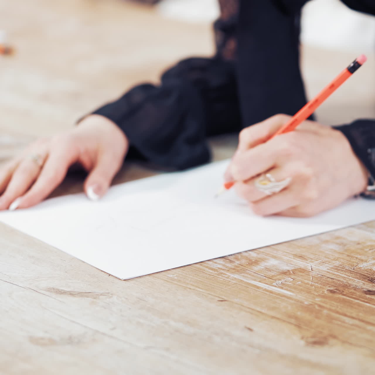 Seamstress draws a sketch of a stylish dress on the wooden background. Woman's hands are making a pattern of a future clothing with a pencil in atelier. Feminine hobby.