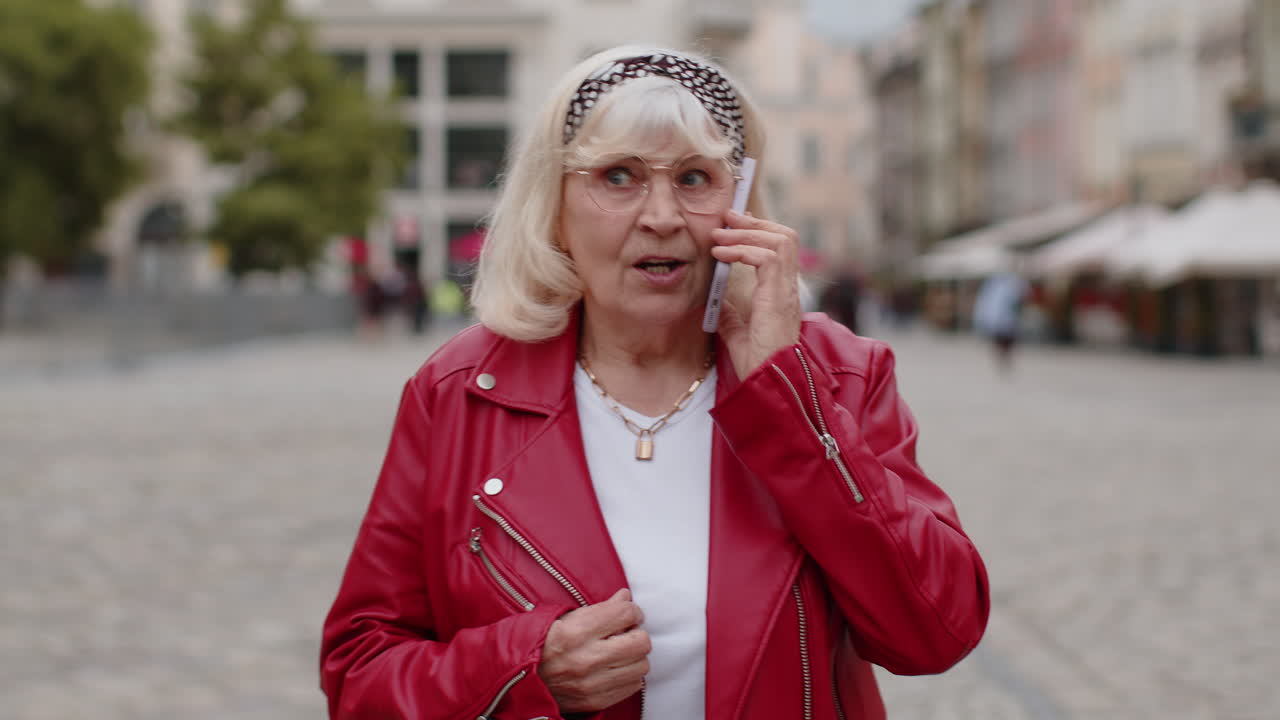 Happy senior woman having remote conversation talking on smartphone good news gossip in city street