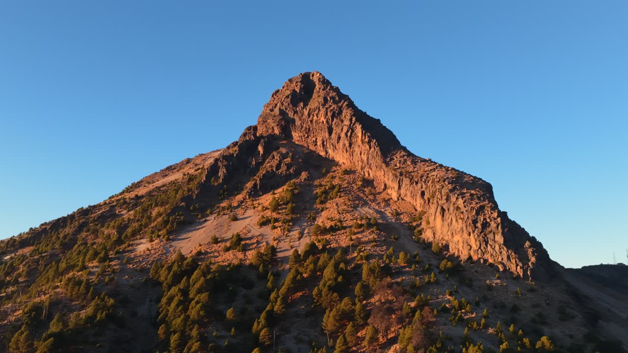 Cima rocciosa del Nevado de Colima (Zapotépetl) illuminata dalla calda luce dell'ora d'oro con vegetazione rada su pendii ripidi in Jalisco, Messico