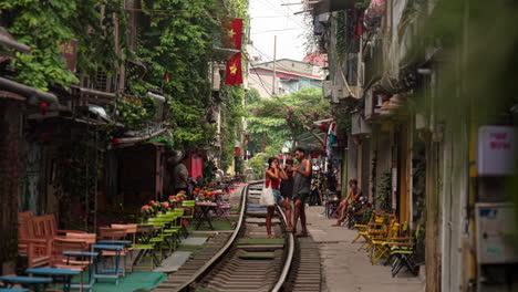 foreign travelers clicking photographs posing at railroad track of famous hanoi train street with cafes and shops, static shot