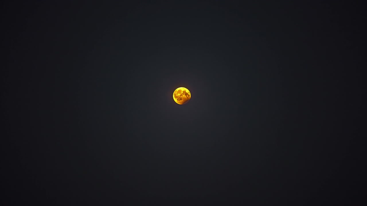 Time lapse shot of golden full moon rising up against dark sky during night