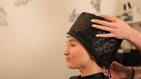 Client Receiving Thermal Cap Treatment During Hair Care Session. A client relaxes with a thermal cap treatment, allowing deep conditioning products to absorb and restore hair health in a professional salon