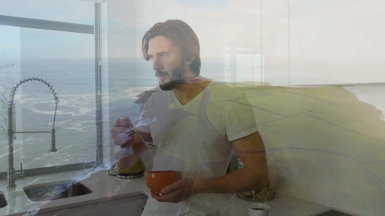 Uomo al bancone che porta il cucchiaio alla bocca, valutando il cibo, facendo una pausa, mescolando, con onde oceaniche sovrapposte.