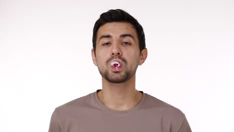 European-dark-haired-young-bristled-man-blowing-chewing-gum-bubble-with-eyes-wide-open-isolated-over-white-background.-Chewing-gum-bursts.-Slow-motion