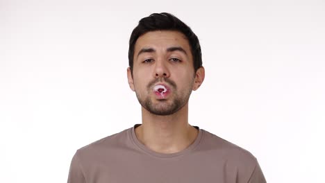 european dark haired young bristled man blowing chewing gum bubble with eyes wide open isolated over white background. chewing gum bursts. slow motion