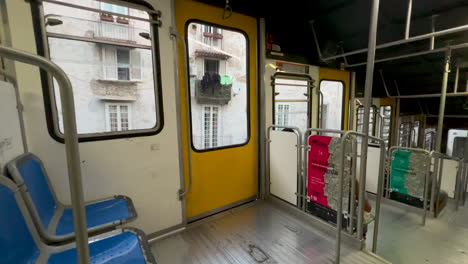 interior of an empty tram with blue seats and yellow doors, city buildings visible through the window