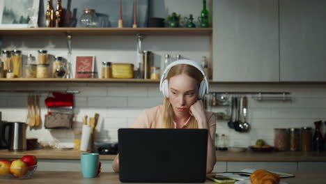 programadora trabajando con una computadora portátil en auriculares sentada en la mesa de la cocina de cerca