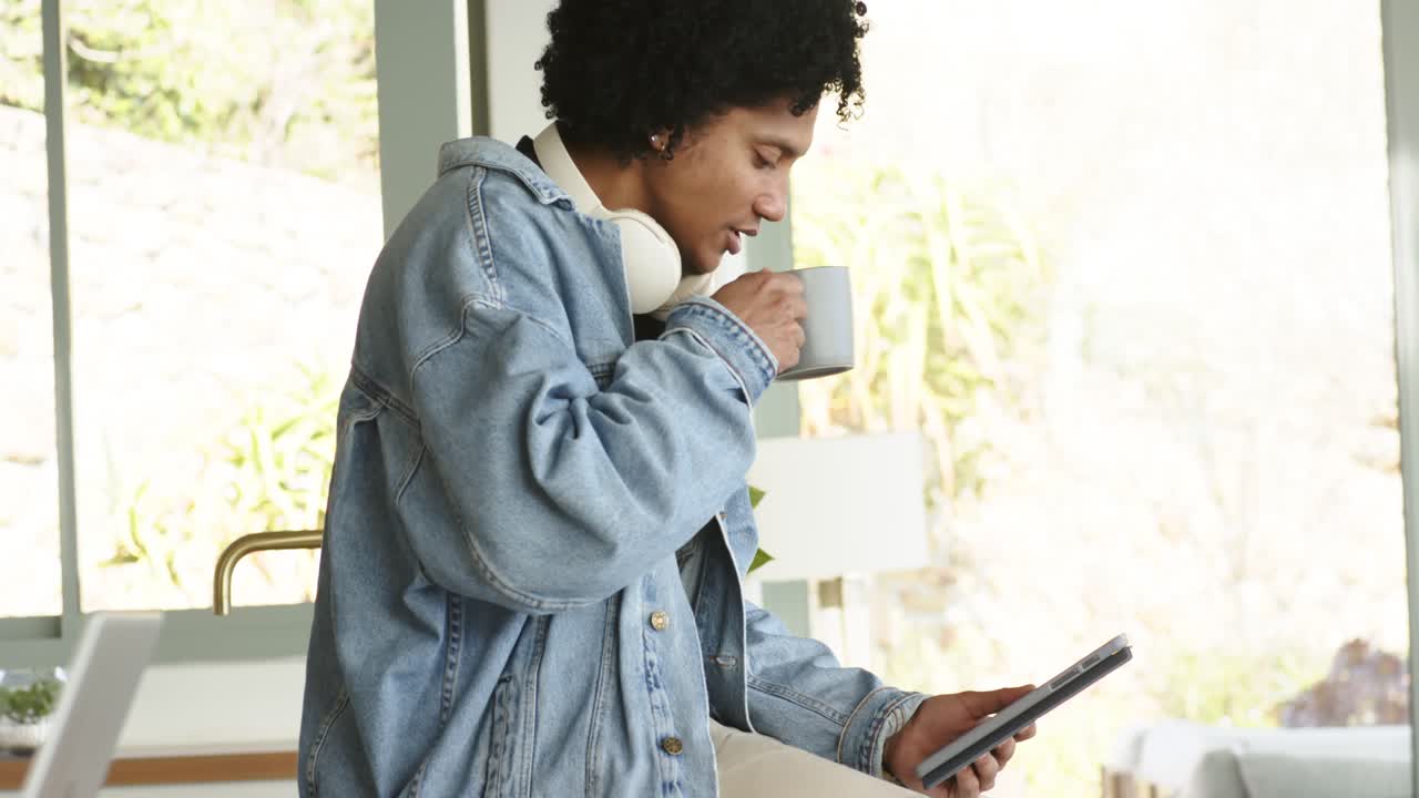 African American man tapping tablet and sipping coffee at kitchen counter focusing on reading