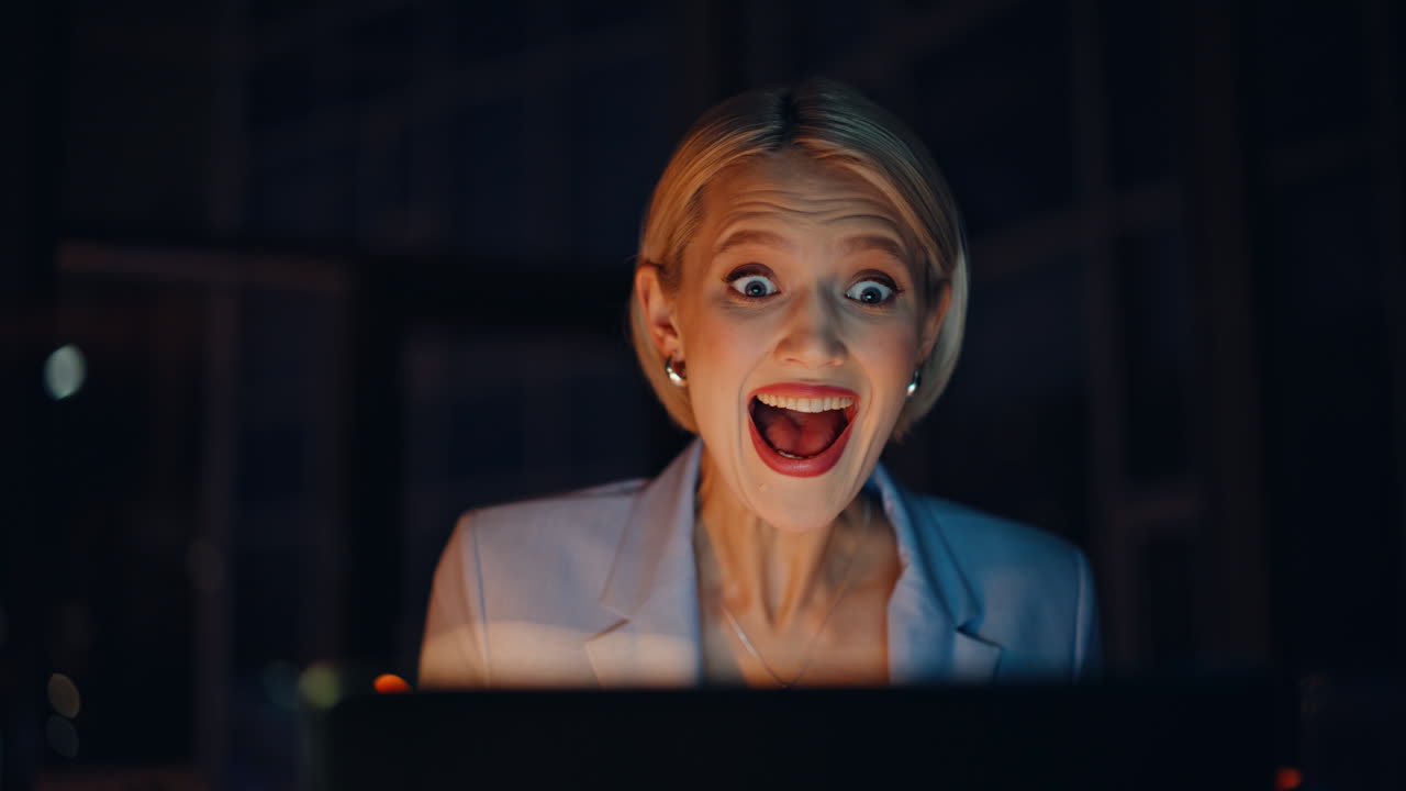 Blonde businesswoman working late evening at dark apartment. Startuper rejoicing