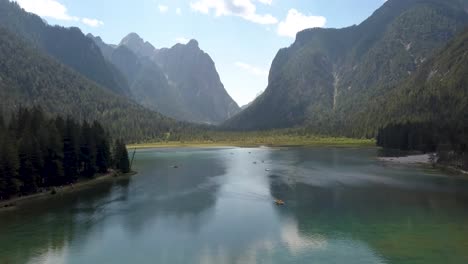 Aerial-in-between-2-pine-trees,-at-summer-lake-Toblachersee-and-mountains-in-the-Alps,-Dolomite-in-Italy,-Europe