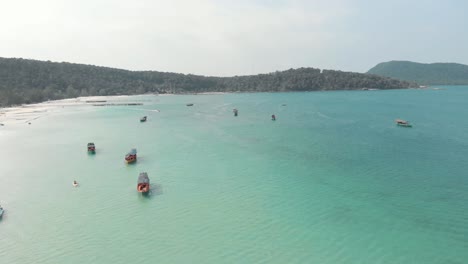 Barcos-De-Pesca-Rural-Camboyanos-De-Madera-Descansando-En-La-Exótica-Bahía-Sarracena-Turquesa-En-Koh-Rong-Sanloem,-Camboya---Toma-Panorámica-Aérea