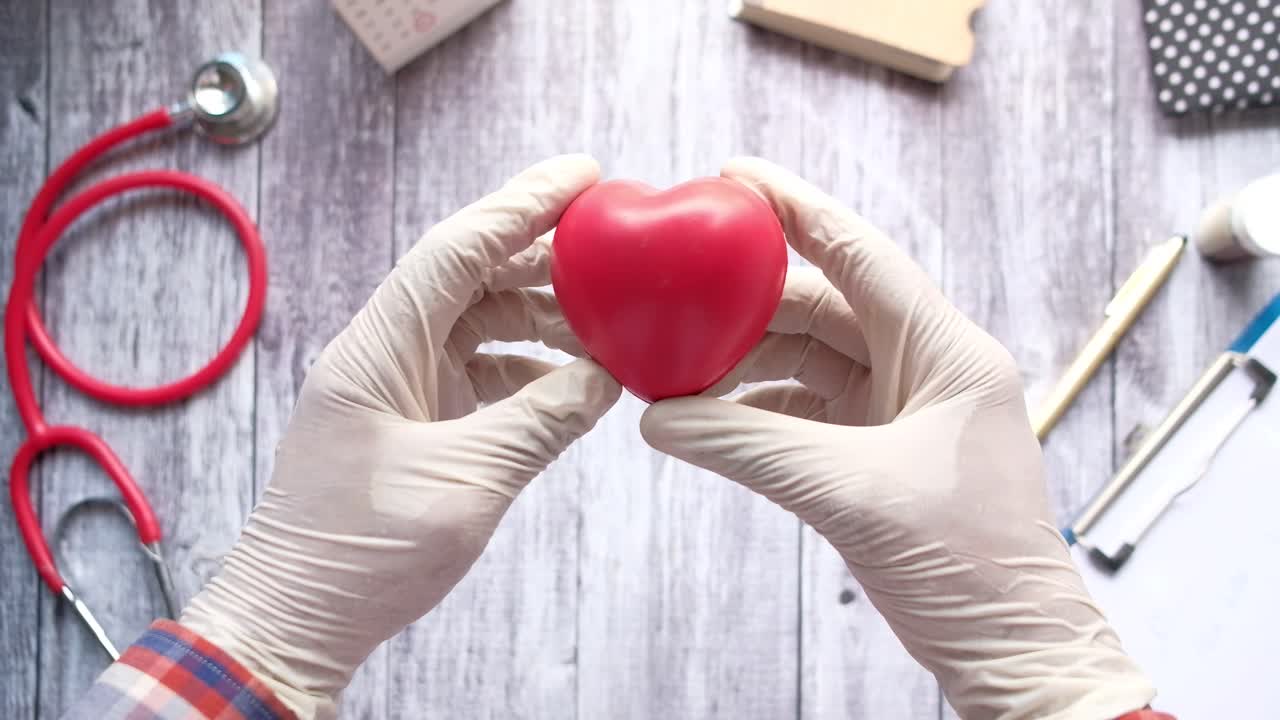 médico con un corazón rojo en guantes médicos