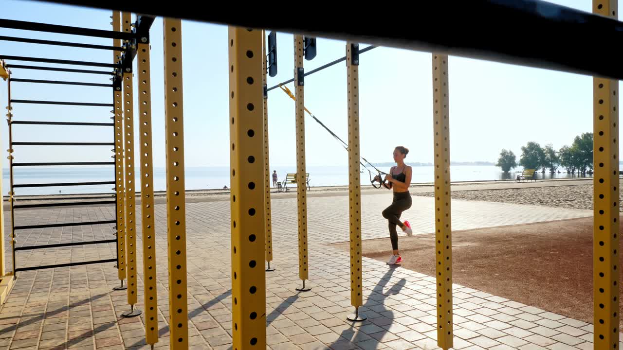 entrenamiento al aire libre. correas de suspensión. entrenamiento con correas. mujer joven atlética está haciendo ejercicios de resistencia de todo el cuerpo usando cuerdas en bucle trx, en la playa durante la puesta o el amanecer. entrenamiento de fitness al aire abierto. concepto de estilo de vida saludable. deporte matutino
